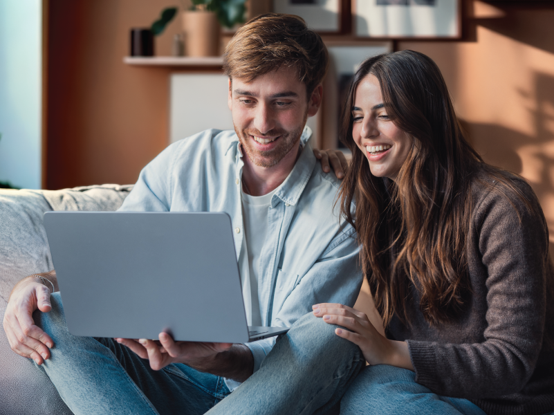 A man and woman sitting on the couch using a laptop.