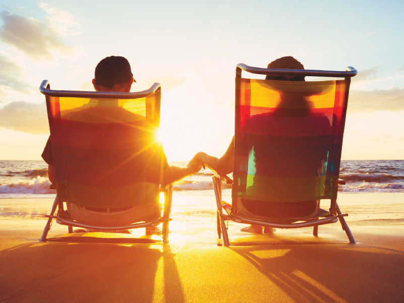 An image of a couple sitting in chairs on the beach and holding hands.