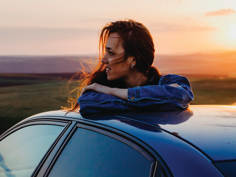 A woman enjoying a sunset in her car. 