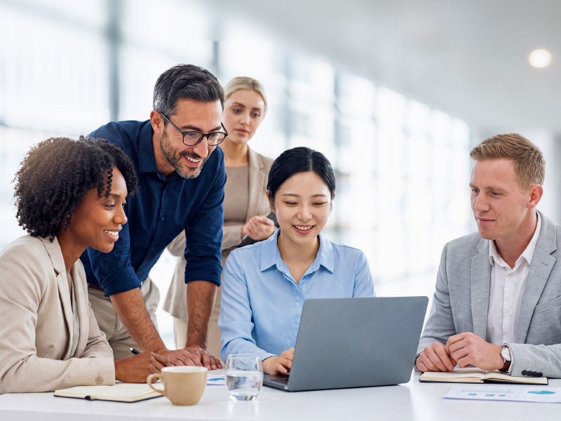 A group of business professionals gathered around a computer.