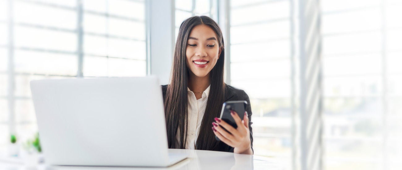 A woman sitting in front of a computer holding a phone.