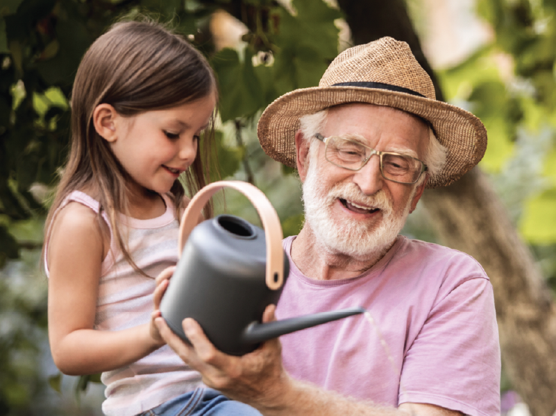 An image of a grandfather and his granddaughter watering plants.