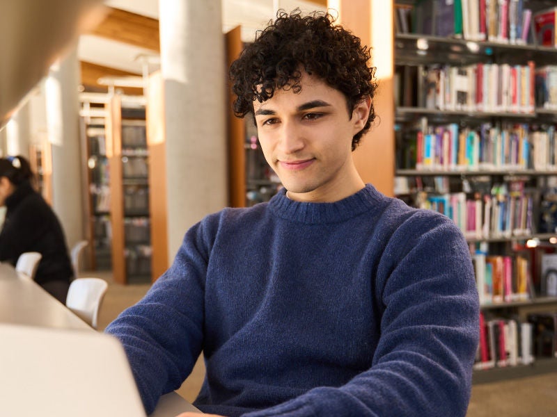 An image of a young man in a library studying.