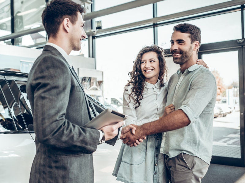 a man and woman shaking hands with a car dealer
