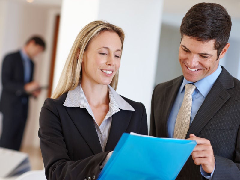 A man and woman in office attire reading a file.