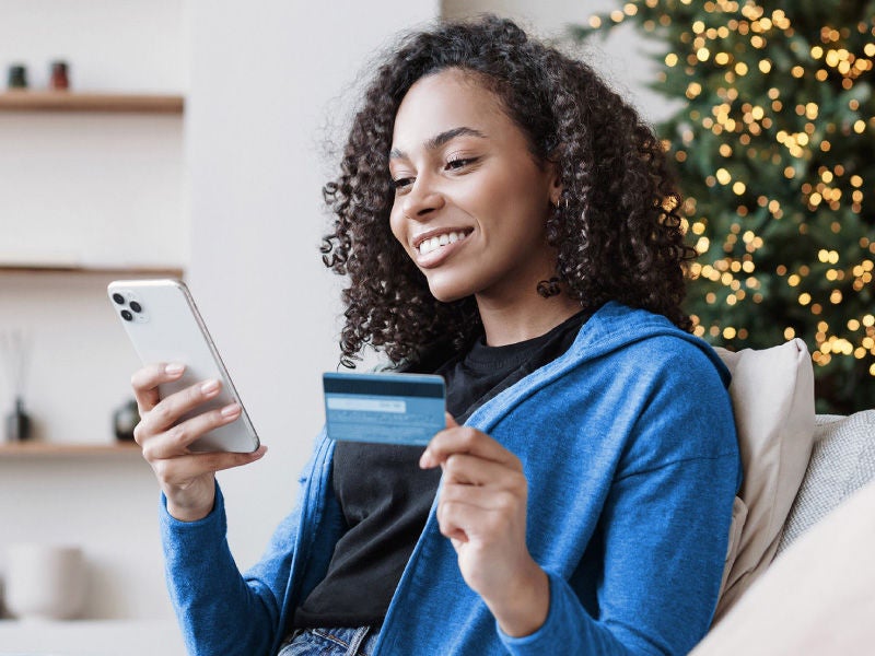 An image of a woman holding a credit card in one hand and a smartphone in the other.