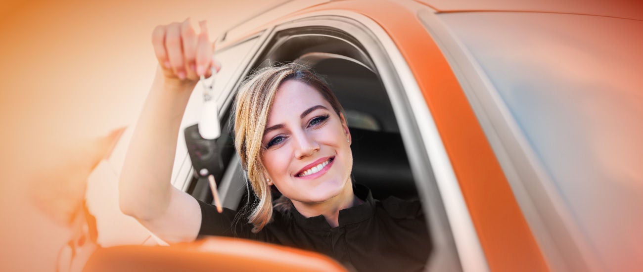 A woman sitting in a new car holding a set of keys.
