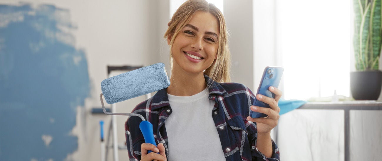 an image of a woman holding a paint roller and a smartphone.