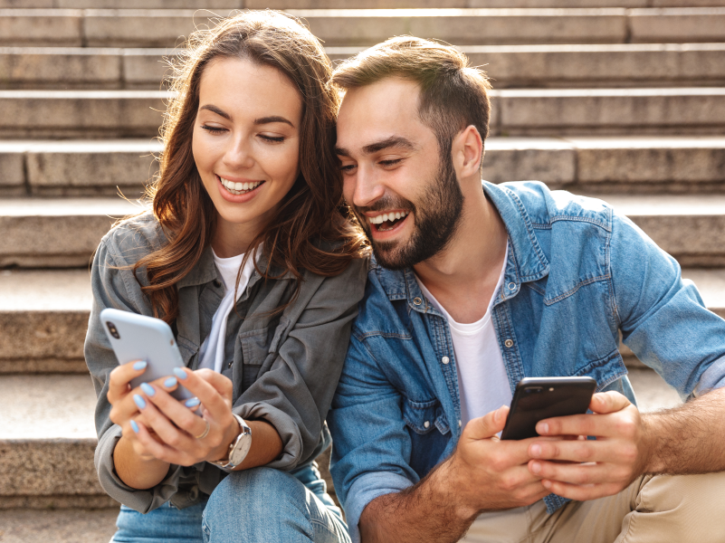 A man and woman looking at a smartphone and smiling.