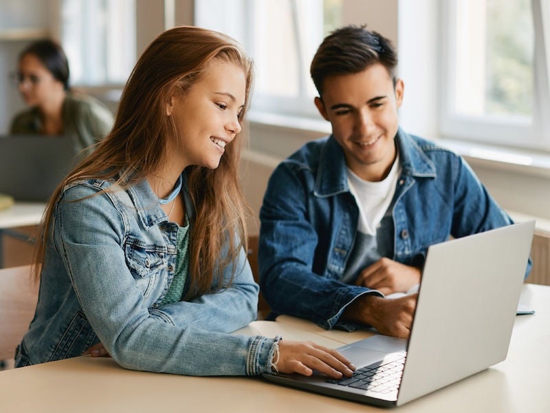 An image of two teens on a laptop smiling.