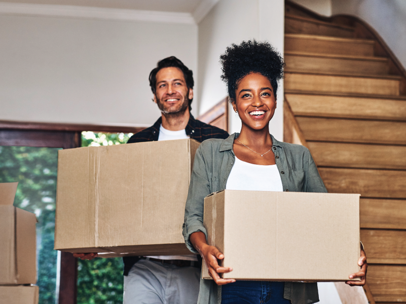a couple carrying boxes into their new home