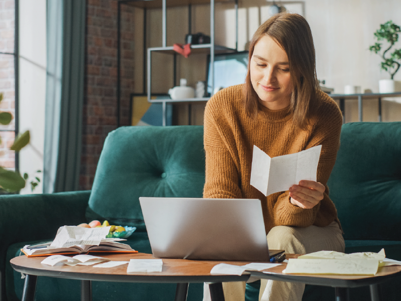 An image of a woman on a laptop holding a piece of paper.