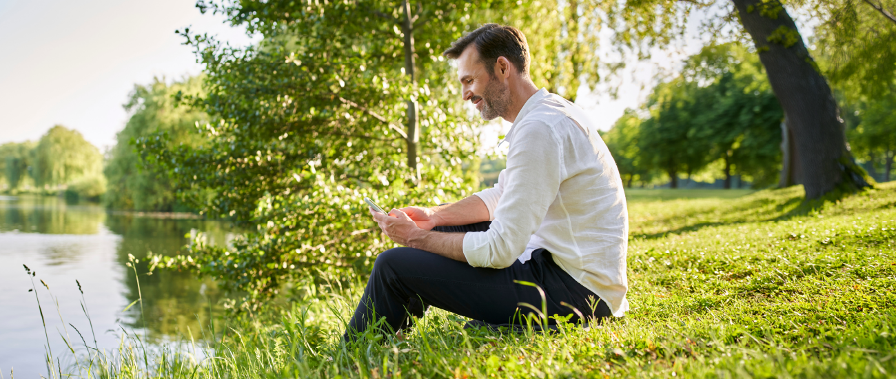 A man sitting by a lake on a smartphone.