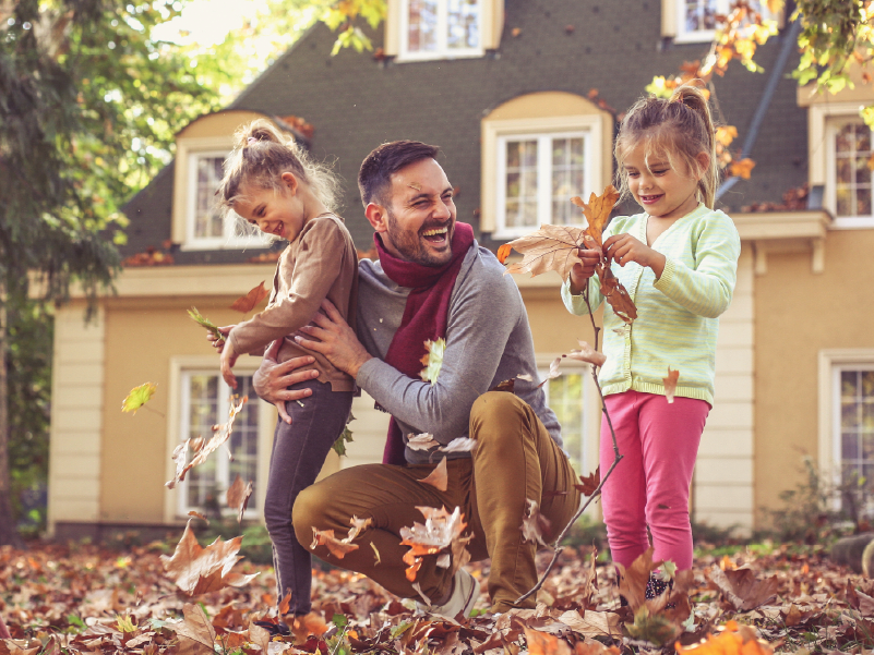 An image of a father playing in the fall leaves with his two daughters.