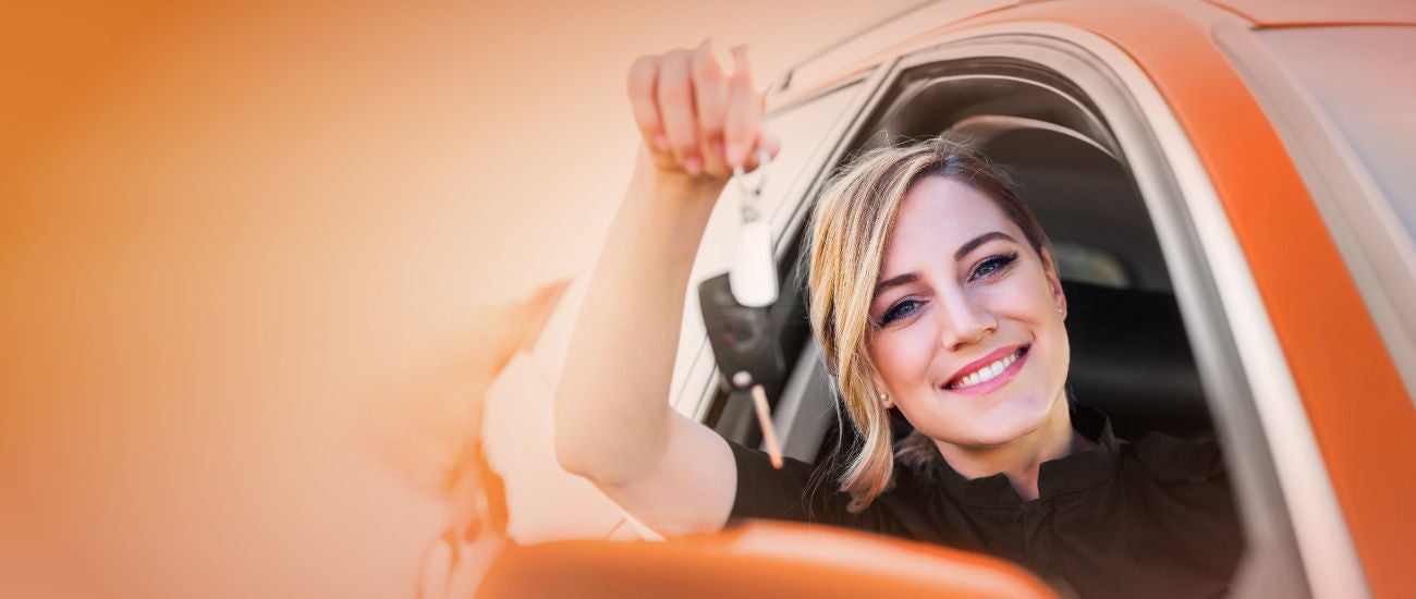A woman sitting in a new car holding a set of keys.