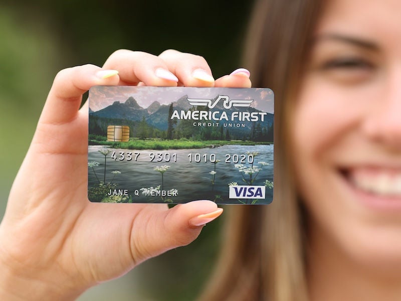 An image of a teenage girl holding up a custom debit card from America First Credit Union.
